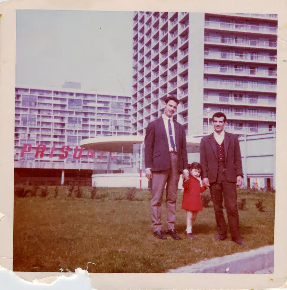 Deux hommes et une petite fille posent devant une tour et le centre commercial d'un grand ensemble