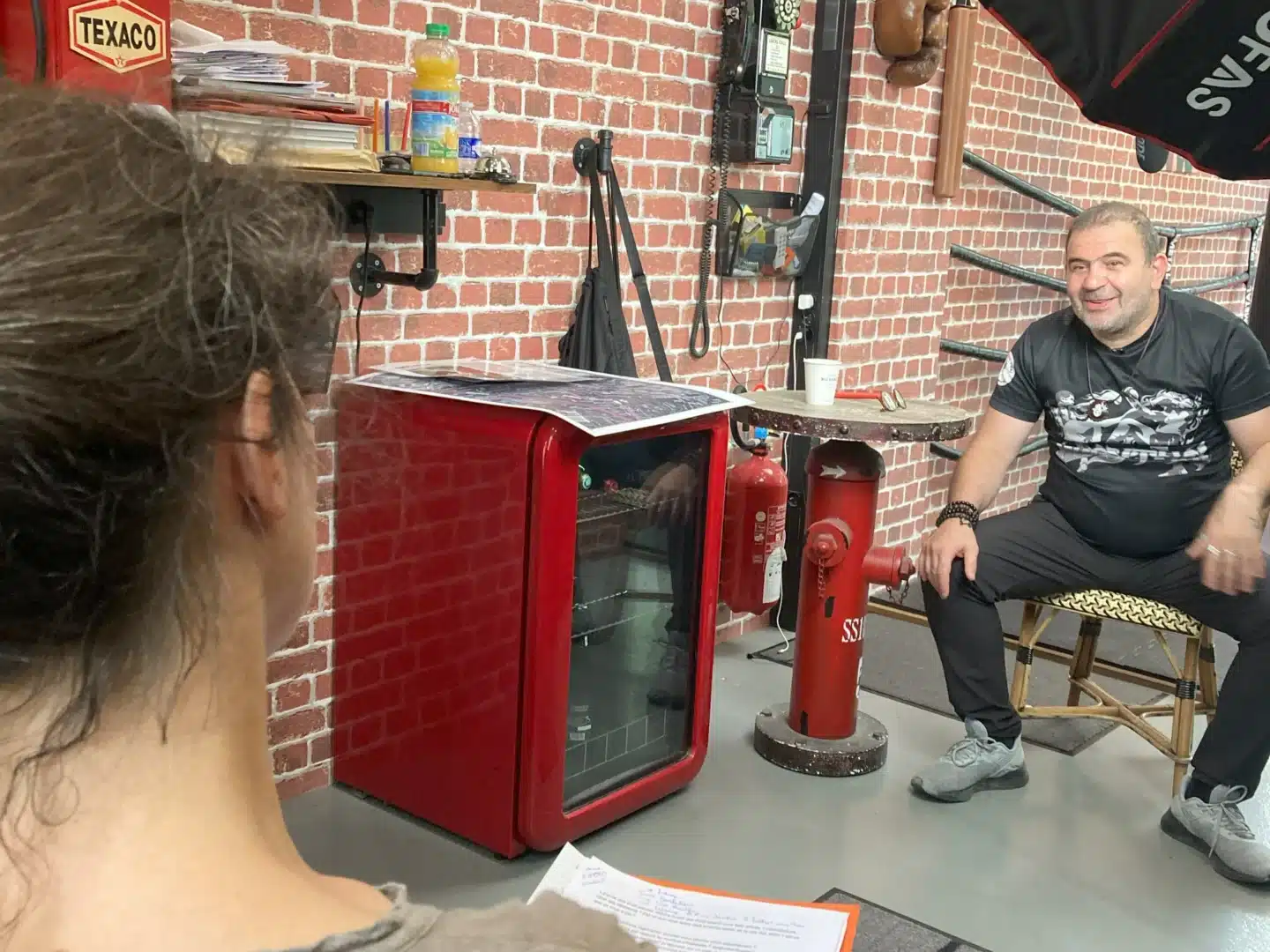 Scène de tournage d'un témoignage. Discussion entre une chercheuse et un témoin, dans une salle de boxe.