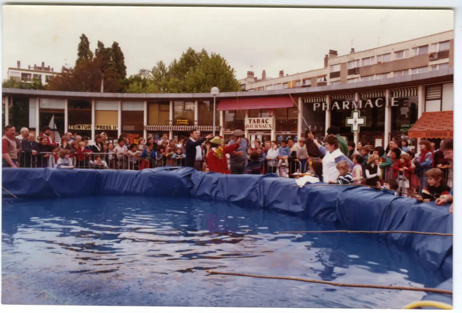 Photographie en couleur d'une foule rassemblée autour d'une piscine installée sur une place publique pour une fête de quartier.