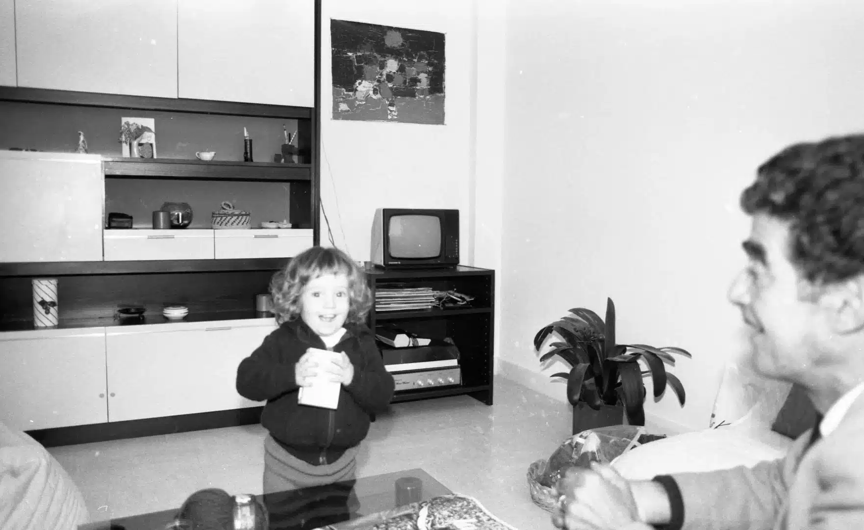 Un homme assis sur un canapé et un enfant dans le séjour d'un appartement. Photographie en noir et blanc